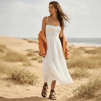Woman wearing a white boho backless tie-back maxi dress with an open back, flowing A-line silhouette, elastic waist, and ankle-length hem on the beach.