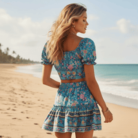 Back view of a boho turquoise floral crop top and mini skirt matching set featuring a smocked back, puff sleeves, elastic waistband, and floral border detail.