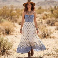 Woman wearing a blue and ivory boho paisley maxi dress with spaghetti straps, a front keyhole neckline, empire waist, and flowing skirt.