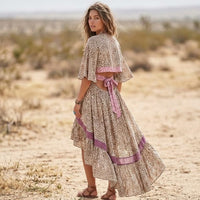 Back view of a leopard print high-low dress featuring an open-back cutout, pink tie bow, empire waist, and flowing maxi-length ruffled hem.