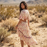 Back view of a beige floral high-low midi dress featuring short flutter sleeves, an open-back cutout, and a flowing ruffled skirt.