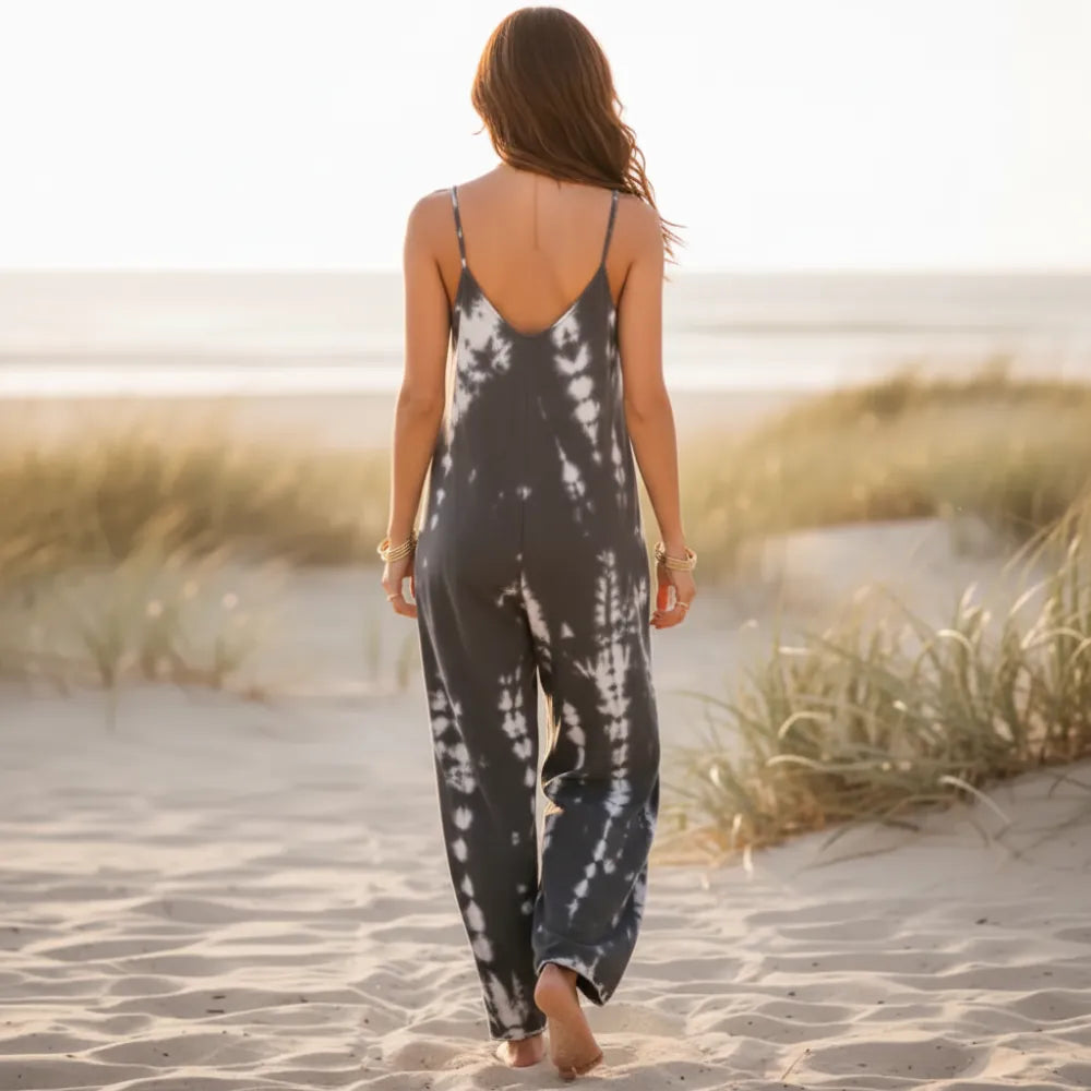 Back of a woman wearing a tie-dye boho wide leg jumpsuit with spaghetti straps, oversized relaxed fit, and flowing full-length pants on the beach.