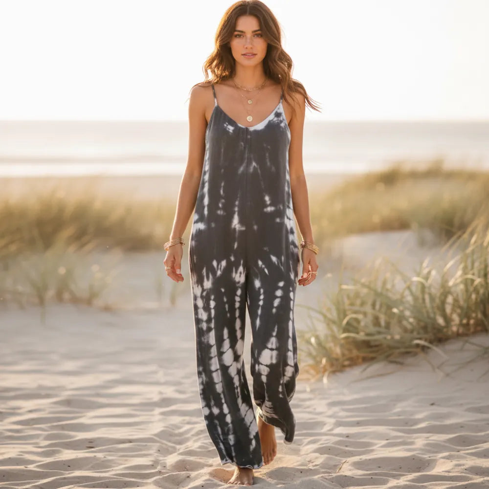 Woman wearing a gray tie-dye boho wide leg jumpsuit with spaghetti straps, oversized relaxed fit, and flowing full-length pants on the beach.