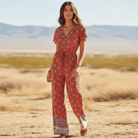 Woman wearing a Red Crimson Bloom boho floral wide leg jumpsuit with pockets featuring a rayon cotton blend, V-neckline, short flutter sleeves, adjustable drawstring waist, front button detail, and wide-leg pants.