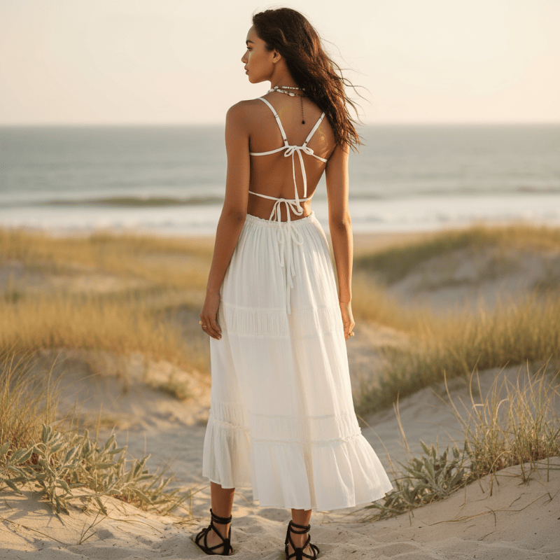 The back of a woman wearing a boho backless tie-back maxi dress with an open back, flowing A-line silhouette, elastic waist, and ankle-length hem on the beach.
