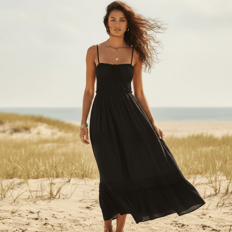 Woman wearing a black boho backless tie-back maxi dress with an open back, flowing A-line silhouette, elastic waist, and ankle-length hem on the beach.