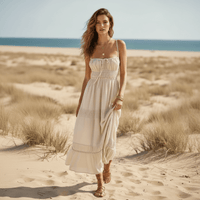 Woman wearing a cream white boho backless tie-back maxi dress with an open back, flowing A-line silhouette, elastic waist, and ankle-length hem on the beach.