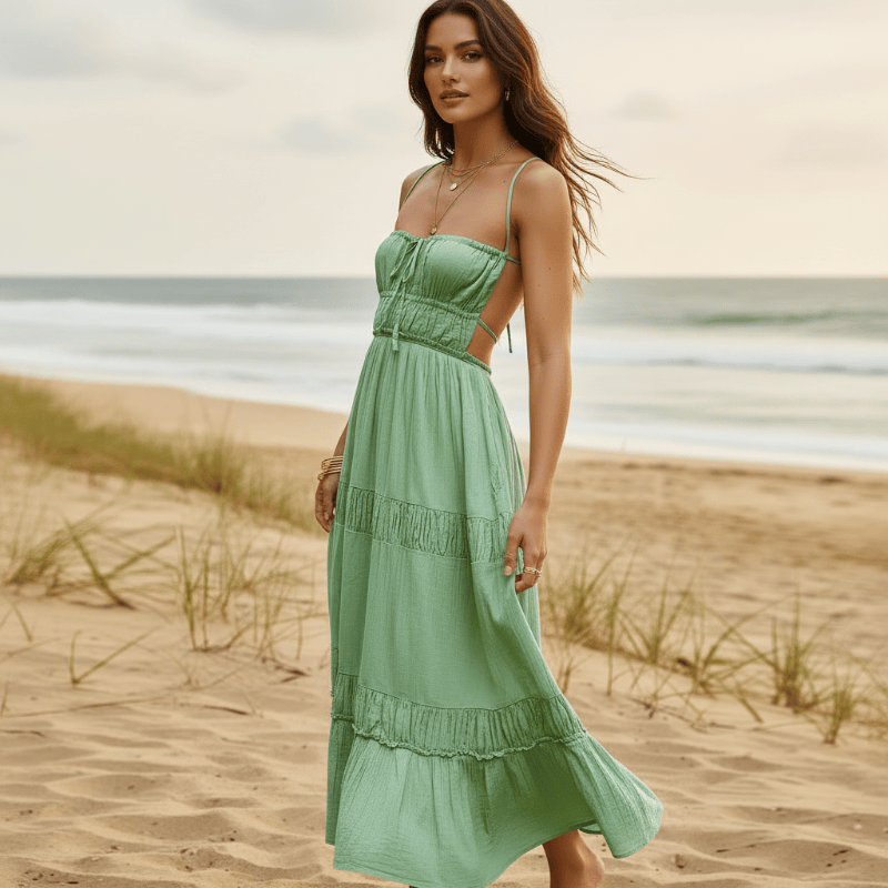 Woman wearing a light green boho backless tie-back maxi dress with an open back, flowing A-line silhouette, elastic waist, and ankle-length hem on the beach.