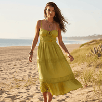 Woman wearing an olive green boho backless tie-back maxi dress with an open back, flowing A-line silhouette, elastic waist, and ankle-length hem on the beach.