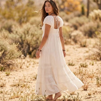 Back view of an off-white cotton maxi dress featuring an open-back cutout, tie closure, puff sleeves, and flowing tiered skirt.