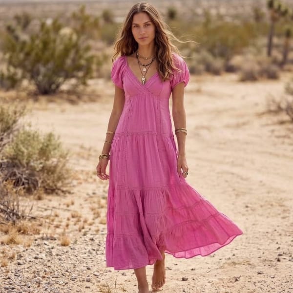Woman wearing a bright pink cotton tiered maxi dress with short puff sleeves, empire waist, and a flowing A-line skirt.