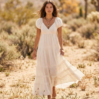 Woman wearing an off-white cotton boho tiered maxi dress with puff sleeves, V-neckline, empire waist, and delicate lace trim.