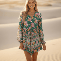 Woman wearing a vintage green floral boho romper with a tassel tie V-neckline, flowy long sleeves, wide-leg shorts, and soft rayon fabric.