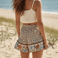 Back of woman wearing Coastal Wildflower boho floral shorts with functional side pockets, a high waist drawstring waistband, lightweight rayon fabric, and a relaxed flowy fit with a vintage-inspired floral border.