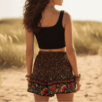 Back of a woman wearing Midnight Meadow black boho floral drawstring shorts with a high-rise elastic waist and colorful floral border paired with a sleeveless black crop top.