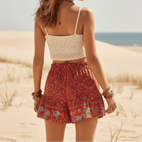 Back of woman wearing Scarlet Blossom boho floral shorts with a high waist drawstring waistband, lightweight rayon fabric, relaxed flowy fit, feminine ruffle hem, and a vintage-inspired floral border in vibrant scarlet red.