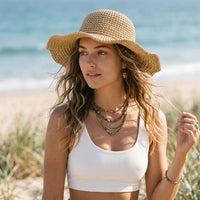 Woman wearing a light khaki crochet-style beach hat with a rounded crown and floppy brim, paired with a white cropped tank and denim skirt.