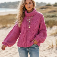 Woman wearing rose red pink boho chunky knit turtleneck sweater with wide sleeves