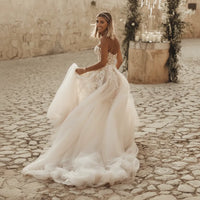 Bride turned around wearing a boho lace wedding dress featuring crystal lace appliqués, sweetheart neckline, off-the-shoulder sleeves, flowing A-line skirt, lace-up corset back, and elegant court train for a romantic outdoor wedding.