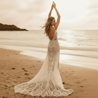 Back of a bride on the beach wearing a white lace A-line wedding dress with a sweetheart neckline, long lace sleeves, floral lace detailing, zipper back, and court train.