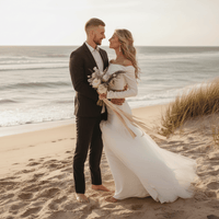 Husband with bride standing sideways wearing a two-piece ivory boho wedding dress with a high neckline, full-length sleeves, ruched detailing, A-line silhouette, zipper back, and flowing court train.