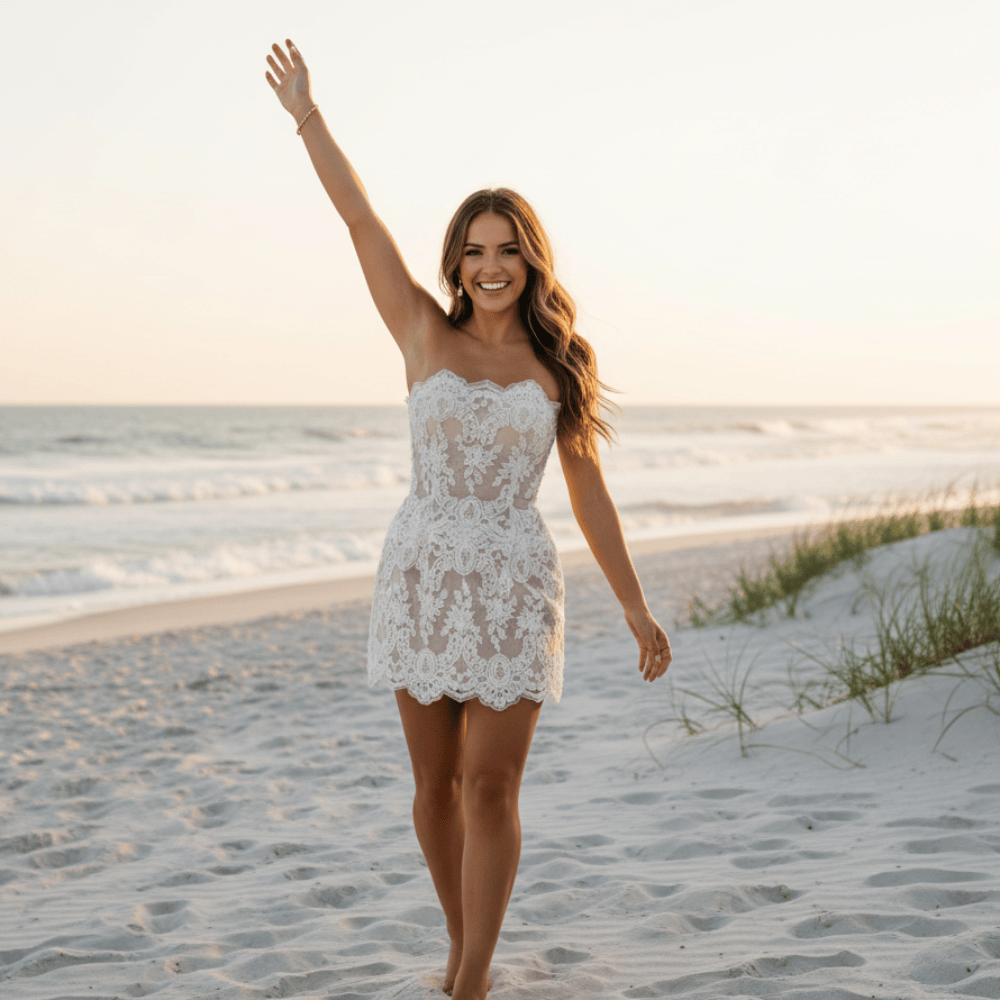 Bride with arms up wearing a white strapless lace wedding dress with floral lace appliqués, pearl and crystal embellishments, sheer mesh detailing, built-in bra, and an elegant mini bridal silhouette.