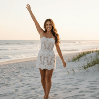 Bride with arms up wearing a white strapless lace wedding dress with floral lace appliqués, pearl and crystal embellishments, sheer mesh detailing, built-in bra, and an elegant mini bridal silhouette.