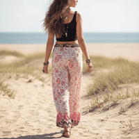 Back of woman wearing Blush Blossom boho wide leg pants with functional side pockets, a high waist drawstring waistband, lightweight rayon fabric, and a flowy floral palazzo silhouette featuring a pink floral and paisley print.