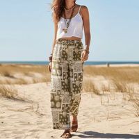 Woman wearing olive mosaic boho wide leg pants with a high waist drawstring waistband, vintage patchwork print, and flowy palazzo silhouette styled with a white tank top.