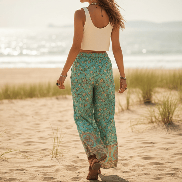 Back of a woman wearing turquoise floral boho wide leg pants with functional side pockets, a high waist drawstring waistband, lightweight rayon fabric, and a flowy palazzo silhouette styled for a beach vacation.