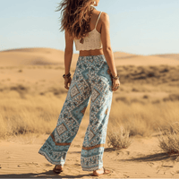 Back of a woman wearing turquoise mosaic boho wide leg pants with functional side pockets, a high waist drawstring waistband, lightweight rayon fabric, and a flowy palazzo silhouette styled for a beach vacation.