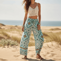 Woman wearing turquoise mosaic boho wide leg pants with functional side pockets, a high waist drawstring waistband, lightweight rayon fabric, and a flowy palazzo silhouette styled for a beach vacation.